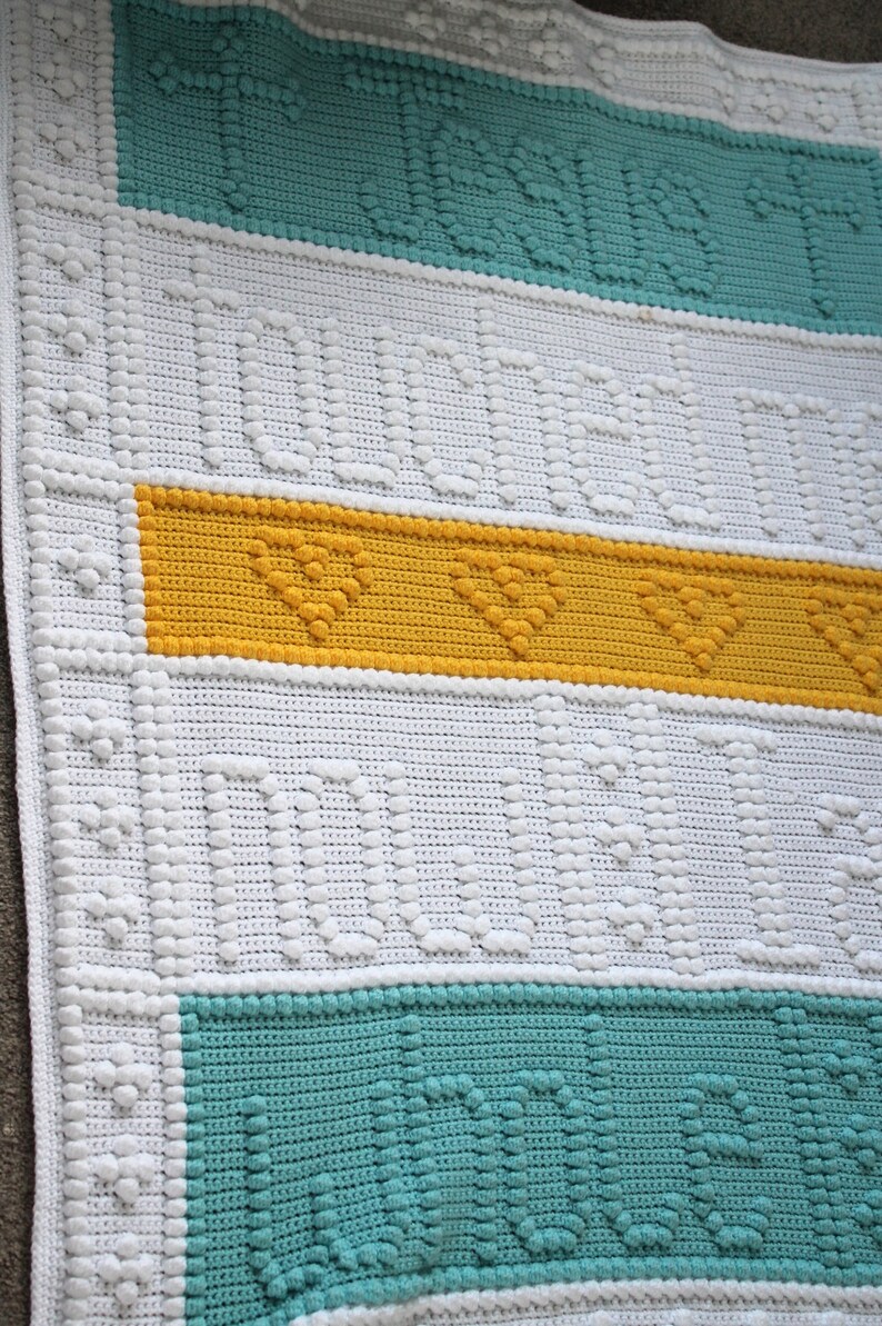 May include: A white crocheted baby blanket with a yellow, teal and white striped pattern. The blanket has a textured design with raised bumps.