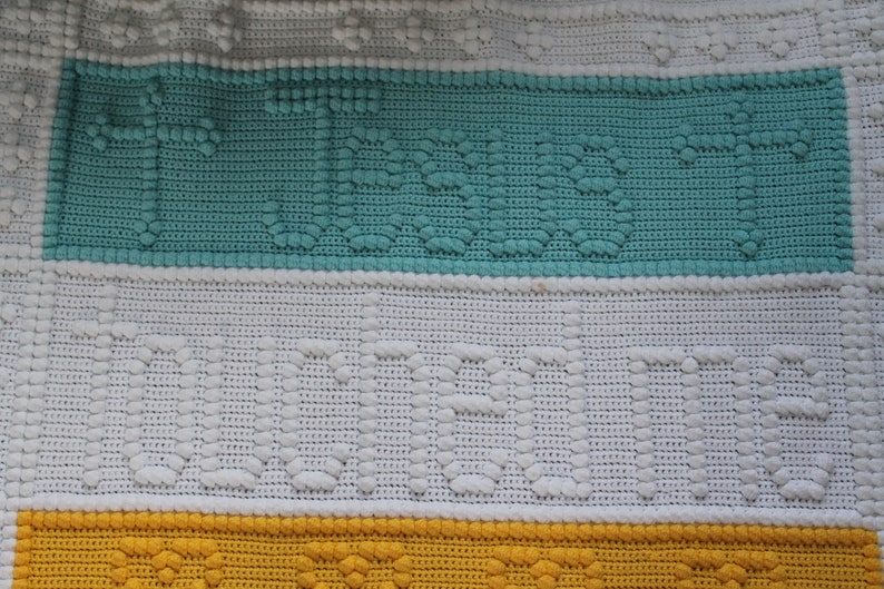 May include: A crocheted blanket with three horizontal stripes. The top stripe is teal, the middle stripe is white, and the bottom stripe is yellow.