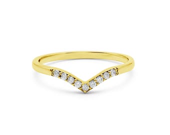 May include: A gold-colored chevron ring with a row of small, clear gemstones set along the V-shaped band. The ring is set against a white background, highlighting its design and sparkle. This ring is a piece of jewelry.