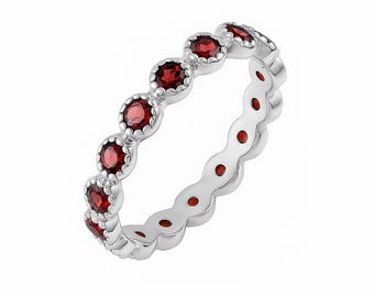 May include: A silver ring featuring a continuous row of round, red gemstones. The ring has a decorative, scalloped edge. The gemstones are a rich red hue and are set evenly around the band. The ring is a piece of jewellery.