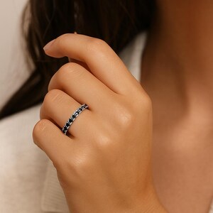 May include: A silver ring set with black gemstones. The ring is on a finger. The gemstones are small and evenly spaced. The ring has a simple, elegant design. The ring's band is approximately 0.2 cm wide.