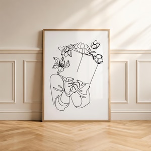 May include: A framed wall art print featuring a black line drawing on a white background. The illustration depicts a person holding an open book in front of their face, with various floral elements blooming from the top of the book.