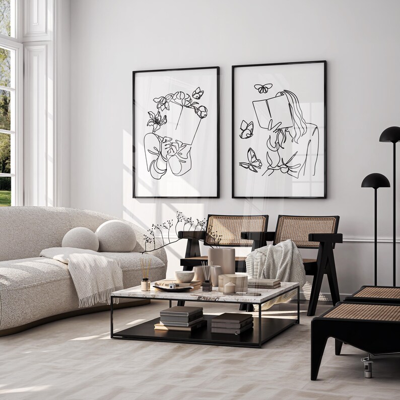 May include: Two framed wall art prints featuring black line drawings on a white background. The left print shows a person holding a book with flowers and butterflies around their head. The right print shows a person reading a book with butterflies.
