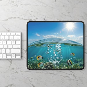 May include: A rectangular mousepad featuring an underwater scene with colorful fish, coral, and bubbles. The top half shows a bright blue sky with the sun shining. The mousepad has a black border and is placed next to a white keyboard.