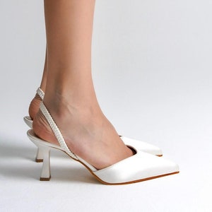 Puede incluir: Tacones blancos de satén con un fino y delicado tirante y punta puntiaguda. Los tacones miden aproximadamente 7,5 cm de alto.