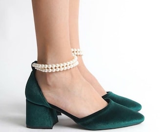 May include: A pair of dark green velvet heeled shoes with a pearl ankle strap. The shoes have a square toe and a block heel.
