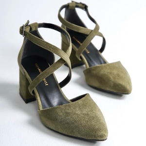 May include: A pair of olive green suede heeled shoes with criss-cross straps and a pointed toe. The shoes have a block heel and a buckle closure.