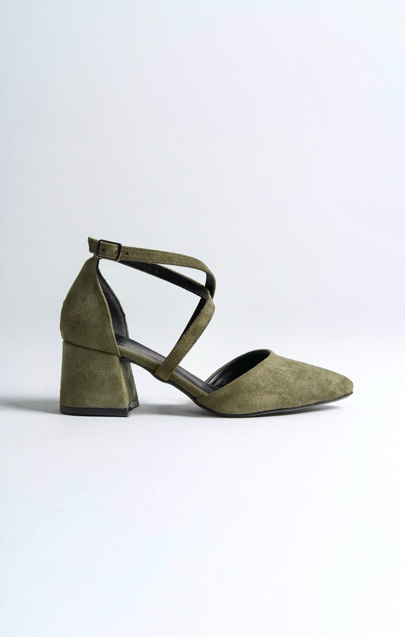 May include: A pair of olive green suede heeled shoes with a criss-cross strap design.