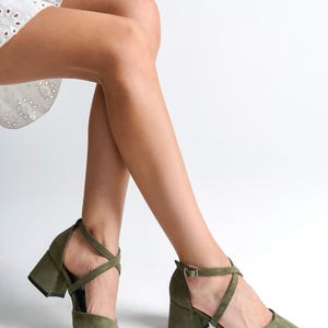 May include: A pair of olive green suede heeled shoes with criss-cross straps and a buckle closure.