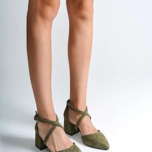May include: A pair of olive green suede heeled sandals with criss-cross straps and a pointed toe.