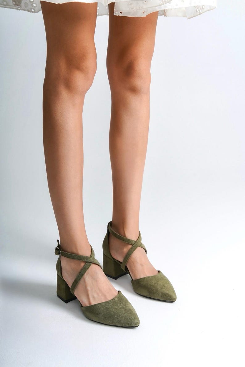 May include: A pair of olive green suede heeled sandals with criss-cross straps and a pointed toe.