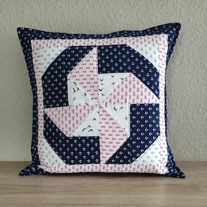 Könnte beinhalten: Dekoratives quadratisches Kissen mit nautischem Thema. Das Kissen hat ein Patchwork-Design mit marineblauen, weißen und roten Stoffen. Das Muster umfasst Anker und Vögel. Das Kissen hat einen marineblauen Rand.