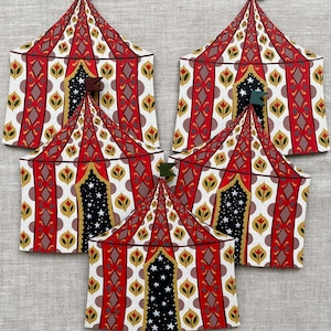 May include: Five decorative circus tent cutouts. The tents have red and white striped roofs with brown and gold accents. The tent doors are black with white stars. Each tent has a small flag at the top, in shades of green and brown.