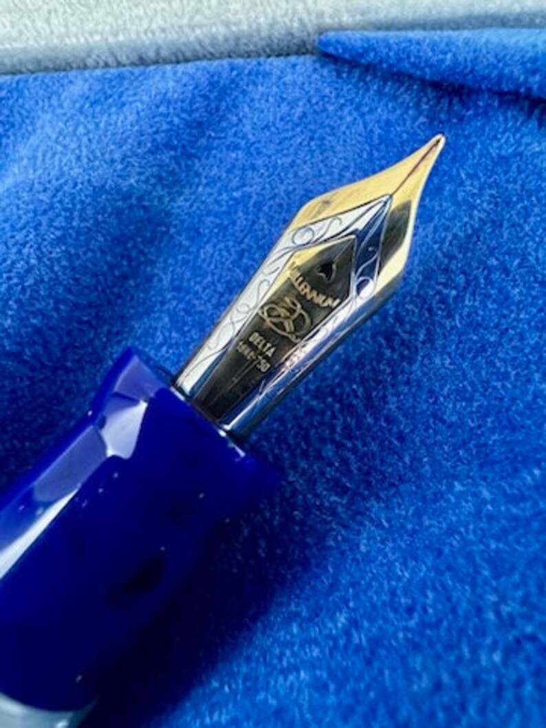 Puede incluir: Primer plano de una pluma de fuente azul y plateada con las palabras "DELTA" e "ITALIA" grabadas en ella.