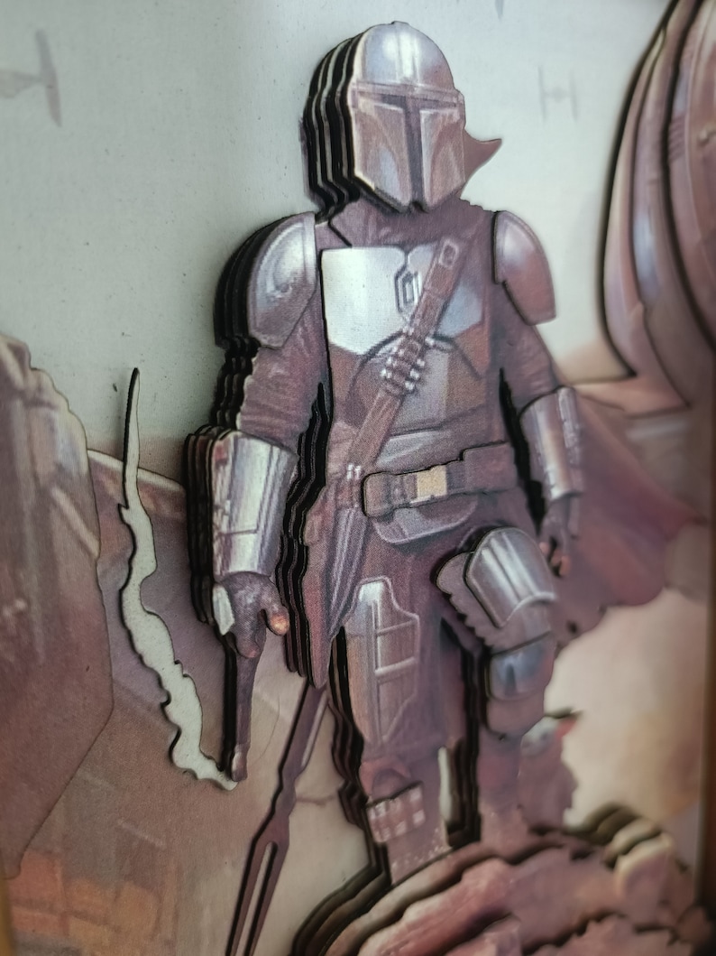 May include: A layered, 3D, wooden art piece of a Mandalorian character from the Star Wars universe. The character is wearing a brown and silver suit with a helmet and a weapon. The background is a brown and beige colour.