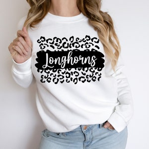 May include: White sweatshirt with a black leopard print design and the word "Longhorns" in black script.