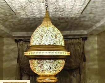 May include: A gold-colored, ornate pendant lamp with a pierced design, hanging from a chain. The lamp has a bulbous shape with intricate cut-out patterns, casting light and shadows. The image includes the "Gates of Morocco" logo.