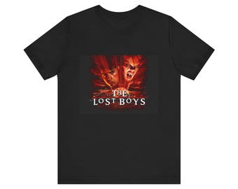 Può includere: T-shirt nera con una grafica di due volti di vampiri dal film "The Lost Boys". La grafica è in rosso e arancione con il titolo del film in bianco.