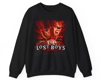 Può includere: Felpa nera con grafica del film "The Lost Boys". Il design presenta due volti, uno con zanne, e il titolo del film in bianco. Lo sfondo è rosso e arancione.