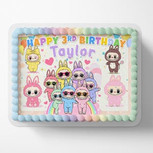 May include: A rectangular cake with a light blue border and colorful frosting. The cake features cartoon characters in bunny costumes, a rainbow, and the text "HAPPY 3RD BIRTHDAY Taylor."