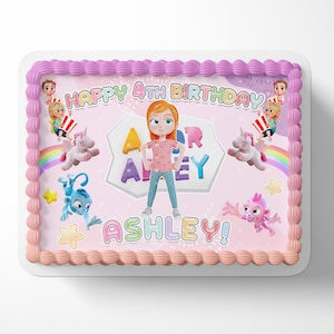 May include: A rectangular birthday cake with pink frosting and decorative borders. The cake features a cartoon girl, unicorns, rainbows, and the text "HAPPY 4TH BIRTHDAY ASHLEY!" in colorful letters. Additional cartoon characters and stars are also present.