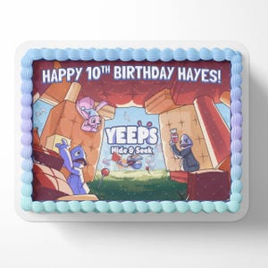 May include: A blue and white birthday cake with a printed image of characters from the game "YEEPS Hide & Seek". The cake is decorated with blue frosting and the text "HAPPY 10TH BIRTHDAY HAYES!"