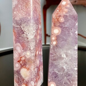 May include: Two amethyst crystal points with a purple and white color pattern. The crystal on the left has a more defined pattern with white and pink accents. The crystal on the right has a more subtle pattern with white and purple accents. Both crystals are labeled A and B.