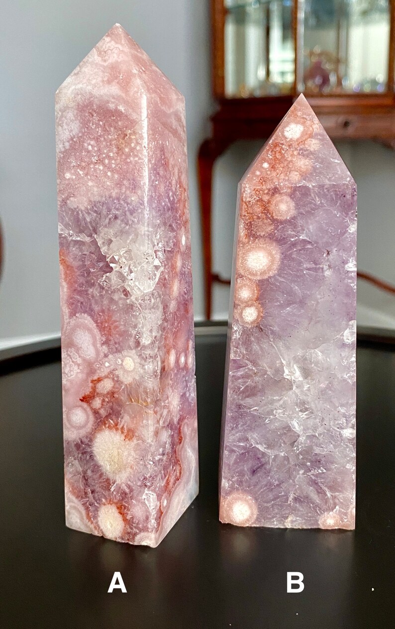 May include: Two amethyst crystal points with a purple and white color pattern. The crystal on the left has a more defined pattern with white and pink accents. The crystal on the right has a more subtle pattern with white and purple accents. Both crystals are labeled A and B.