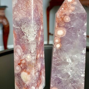 May include: Two amethyst crystal points with a purple and white color pattern. The crystal points are shaped like pyramids and have a smooth, polished surface. The crystal points are labeled A and B.
