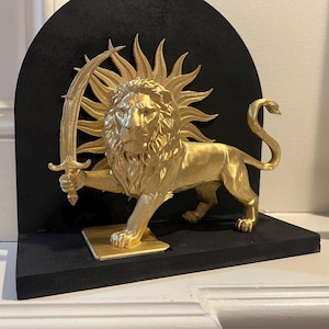 May include: A golden lion statue holding a sword, set against a black backdrop. The lion has a sunburst crown and stands on a gold base. The statue is on a black shelf.
