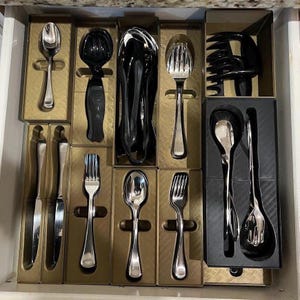 May include: A drawer filled with various silverware pieces, including spoons, forks, and knives. The silverware is arranged in individual compartments, with some pieces having a shiny silver finish and others in black.