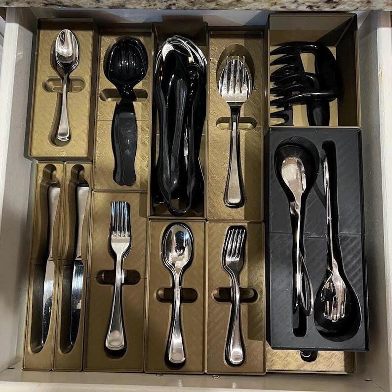 May include: A drawer filled with various silverware pieces, including spoons, forks, and knives. The silverware is arranged in individual compartments, with some pieces having a shiny silver finish and others in black.