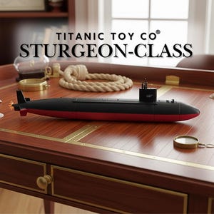 May include: A black and red toy submarine with the text "TITANIC TOY CO® STURGEON-CLASS" on a wooden desk. The submarine has a sleek design with a red bottom and black top. A rope and a magnifying glass are also on the desk.