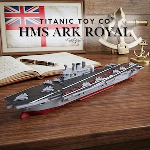 Puede incluir: Maqueta del portaaviones HMS Ark Royal, gris y rojo, con aviones en miniatura en la cubierta. El modelo se encuentra sobre una superficie de madera, con una bandera de la Union Jack enmarcada y el texto "TITANIC TOY CO HMS ARK ROYAL".