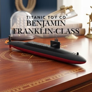 Könnte beinhalten: Ein schwarzes und rotes Modell-U-Boot mit dem Text "TITANIC TOY CO BENJAMIN FRANKLIN-CLASS" auf einer Holzoberfläche. Das U-Boot hat ein schlankes Design mit einem schwarzen oberen Rumpf und einem roten unteren Rumpf. Das Modell ist eine detaillierte Nachbildung.