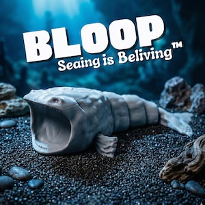 May include: A gray, open-mouthed sea creature sculpture with the word "BLOOP" and the phrase "Sealing is Believing" in white text. The sculpture is on a dark, textured surface with rocks and a blue background.