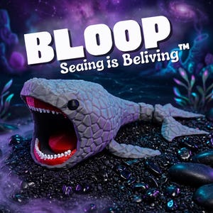 Puede incluir: Un juguete de ballena gris texturizada con la boca abierta que revela detalles rojos y blancos. La palabra "BLOOP" está encima de la ballena, con "Seeing is Beliving" debajo. El juguete está sobre una superficie negra con rocas oscuras.