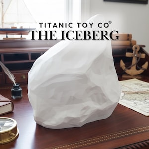 Op de afbeelding: Een witte, geometrische ijsbergsculptuur met de tekst "TITANIC TOY CO THE ICEBERG". De sculptuur staat op een houten bureau met nautische decoratie, waaronder een modelzeilboot en een anker.