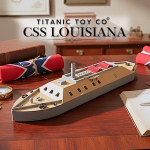 Może przedstawiać: Model CSS Louisiana, pancernika z czasów wojny secesyjnej, na drewnianej powierzchni. Model jest beżowy, szary i czerwony, z tekstem "TITANIC TOY CO" i "CSS LOUISIANA". Obecna jest również zwinięta flaga Konfederacji.