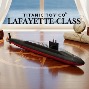 May include: A black and red toy submarine, labeled "LAFAYETTE-CLASS" by "TITANIC TOY CO", rests on a wooden surface. The model features detailed fins and a conning tower. A compass and scroll are in the background.