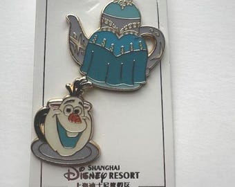 May include: Two Disney enamel pins featuring characters from Frozen. One pin is a teal and silver teapot, and the other is a white and teal Olaf teacup. The pins are on a white card with the Shanghai Disney Resort logo.