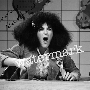 May include: Black and white image of a person with a large afro, wearing a patterned shirt and a blazer. The person is gesturing with their hand and has their mouth open. The background includes a world map and a grid.