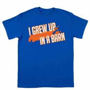 May include: A royal blue t-shirt with an orange outline of Long Island and the text "I grew up in a barn" in white.