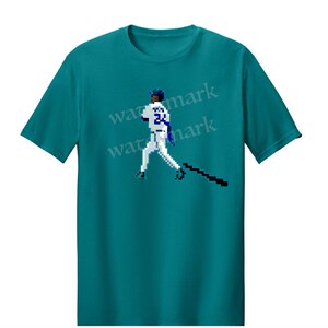 May include: Teal t-shirt featuring a pixelated baseball player in a batting stance. The player is wearing a white uniform with blue accents and the number 24. The design includes a black bat and a blue cap.
