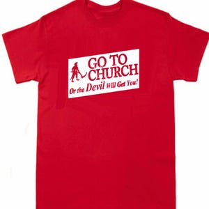 May include: A red t-shirt with a white rectangular graphic. The graphic features a silhouette of a person with a pitchfork and the words "GO TO CHURCH" above the phrase "Or the Devil Will Get You!"