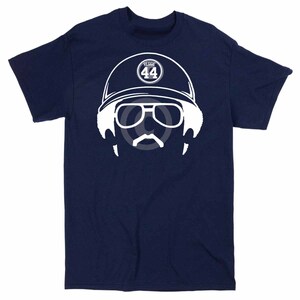 Può includere: Una t-shirt blu navy con una silhouette bianca di una persona che indossa un cappello da baseball con il testo "REGGIE 44" sul davanti. La persona indossa occhiali da sole e ha i baffi.