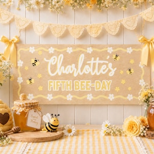 May include: A rectangular tan sign with white daisy borders, yellow bee illustrations, and the white text Charlotte's FIFTH BEE-DAY. The sign is decorated with yellow ribbons on both sides and is surrounded by honey jars and bee-themed decor.