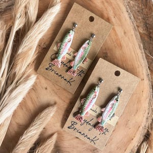 May include: A pair of handmade earrings featuring a realistic painted trout design. The earrings are made with polymer clay and have silver hooks. The earrings are packaged on a brown card with the text "Made with love by Brianna K."