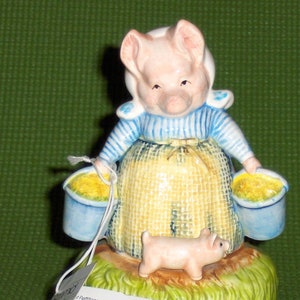 Peut inclure: Une figurine en porcelaine d'un cochon portant une robe bleue et blanche et portant deux seaux de fleurs jaunes. Un petit cochon se tient à côté du gros cochon. La figurine est sur une base verte avec de l'herbe et des fleurs. La figurine est une pièce musicale et porte une étiquette qui dit "Aunt Pettitoes™".