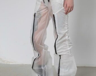 Op de afbeelding: Witte transparante broek met zwarte ritsdetails. De broek is gemaakt van een lichtgewicht, doorschijnende stof en heeft een losse pasvorm.